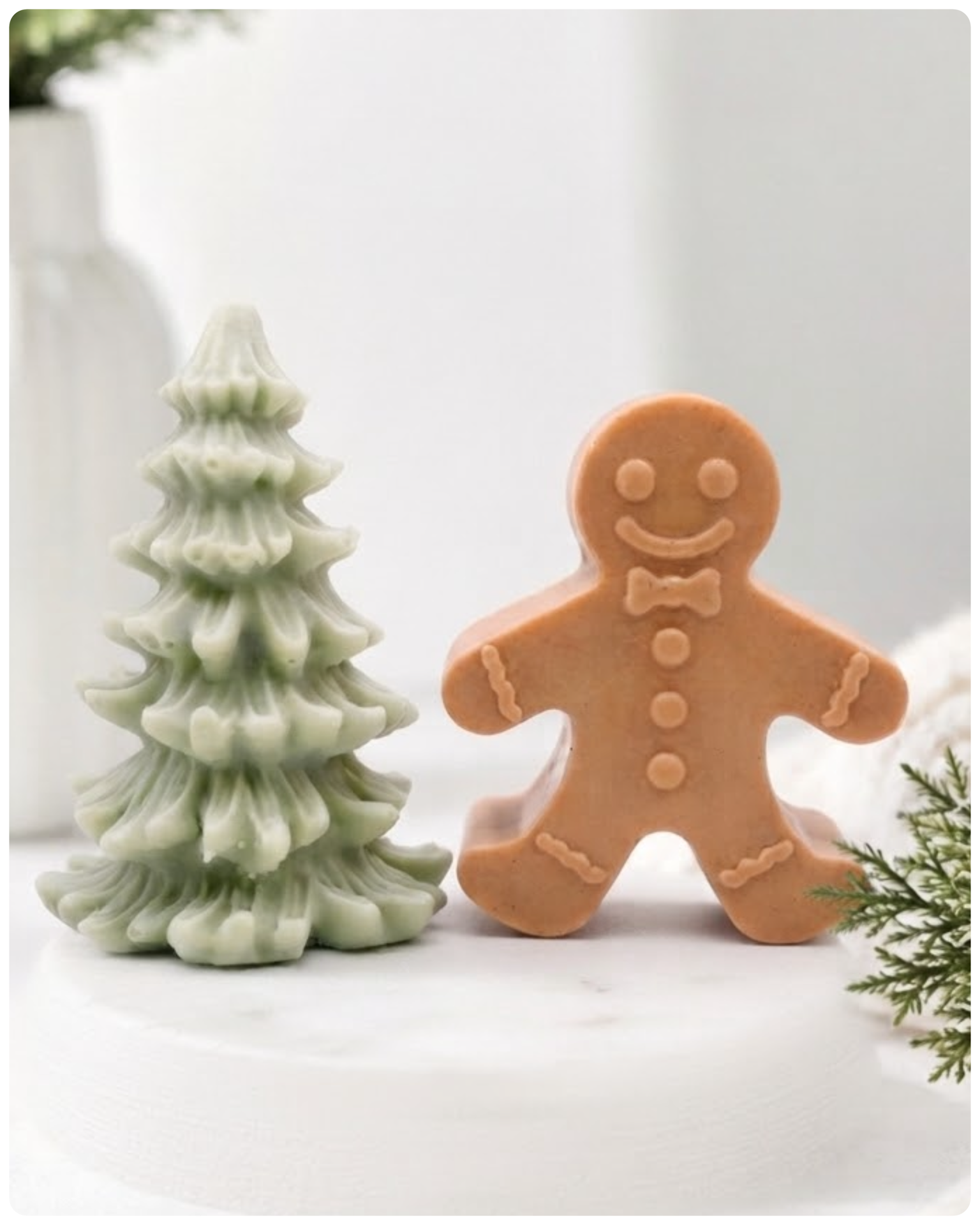 A handmade vegan soap featuring a classic gingerbread man with a smiling face, a bow tie, and decorative icing details on his arms and legs, and a Christmas tree - displayed on a miniature wooden easel.