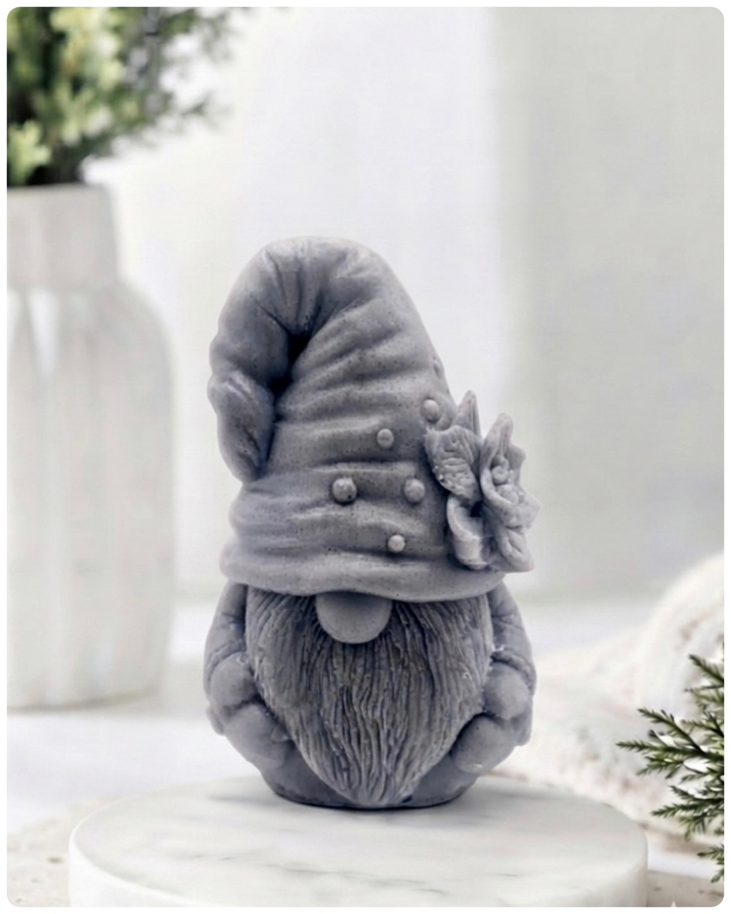 handmade vegan soap in the shape of a garden gnome sculpture with a long beard and a tall hat adorned with a large rose, displayed on a rustic white wooden surface in a bright farmhouse decor setting.