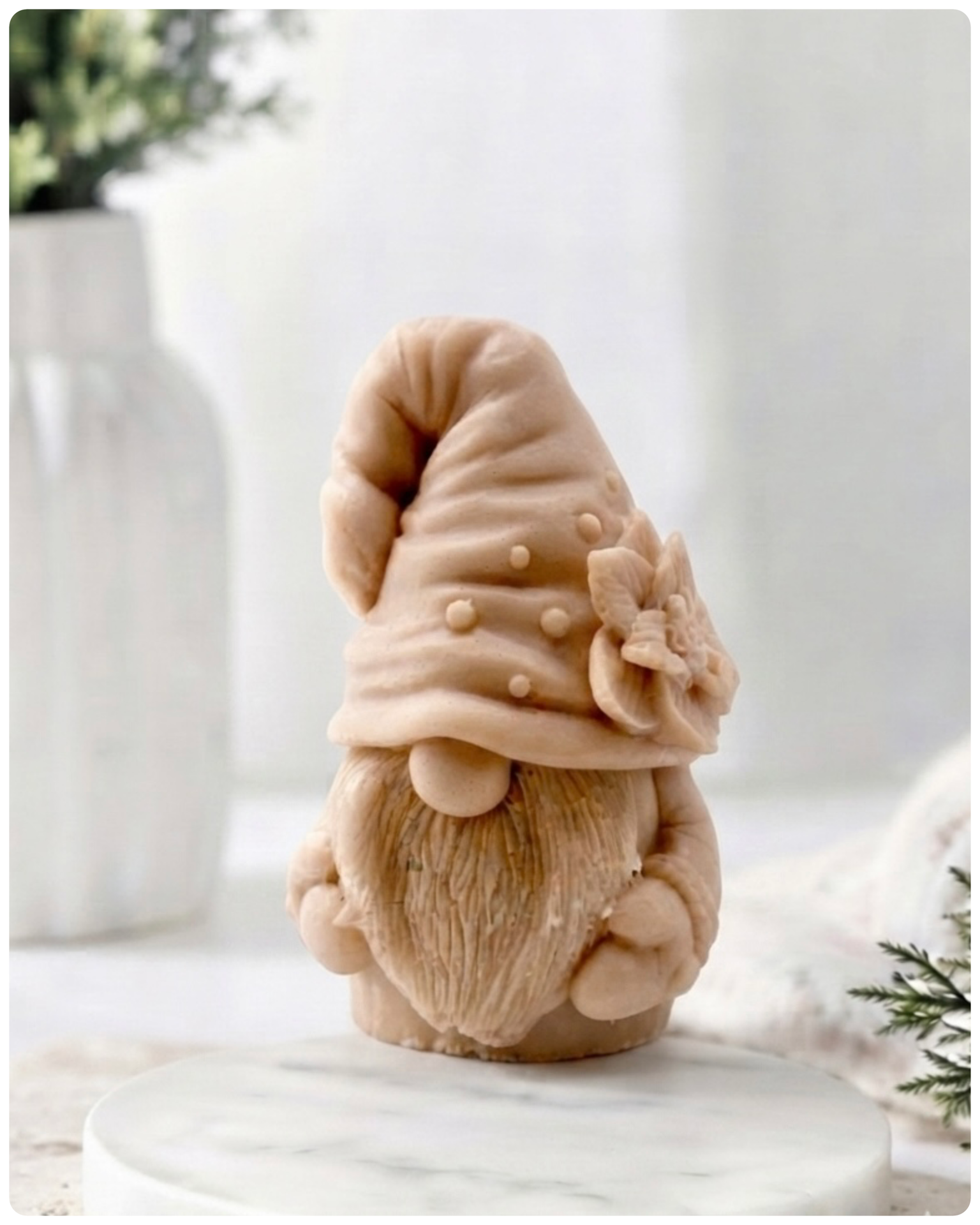 handmade vegan soap in the shape of a garden gnome sculpture with a long beard and a tall hat adorned with a large rose, displayed on a rustic white wooden surface in a bright farmhouse decor setting.