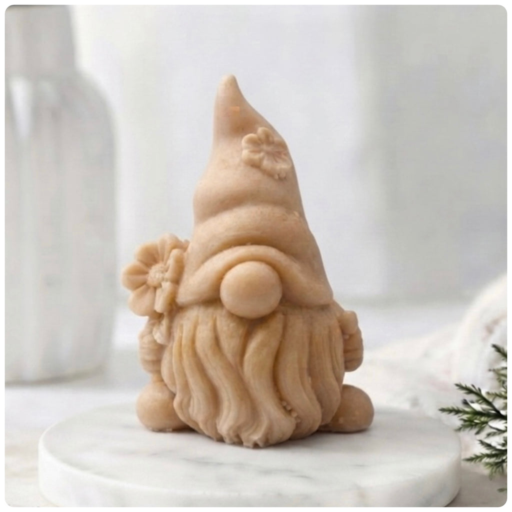 A 3D handmade vegan soap in a warm cream tone, sculpted into a cute garden gnome or gonk with a long flowing beard, a large round nose, and a tall pointed hat adorned with small embossed flowers.
