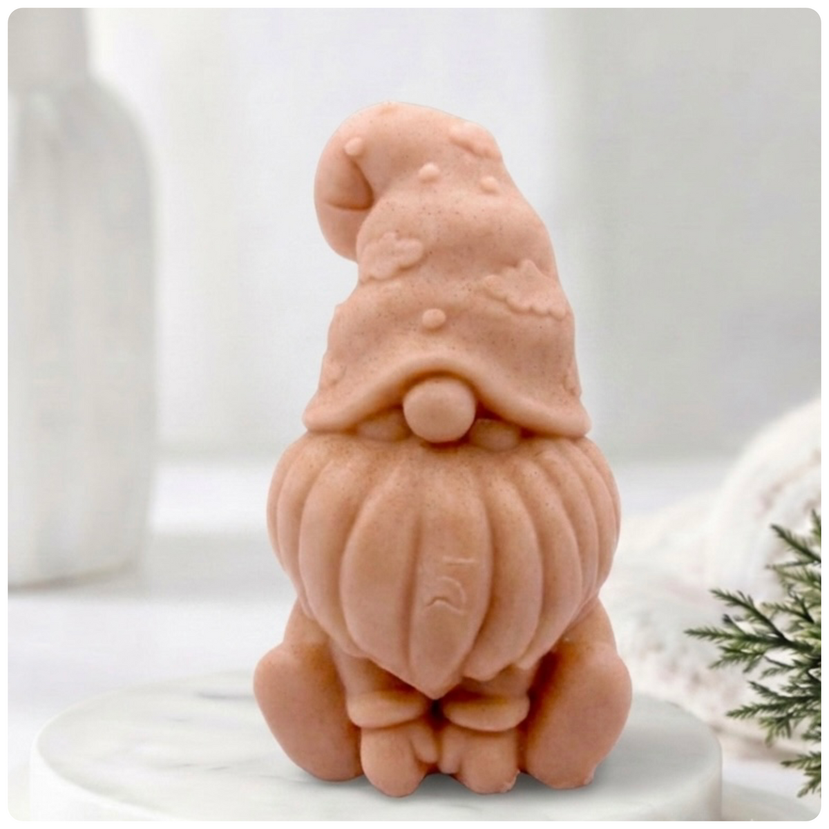 A handmade vegan soap in a natural tone, sculpted as a gnome (gonk) with a tall, curved hat that covers the eyes and has clouds on it, a round nose, and a long, textured beard.
