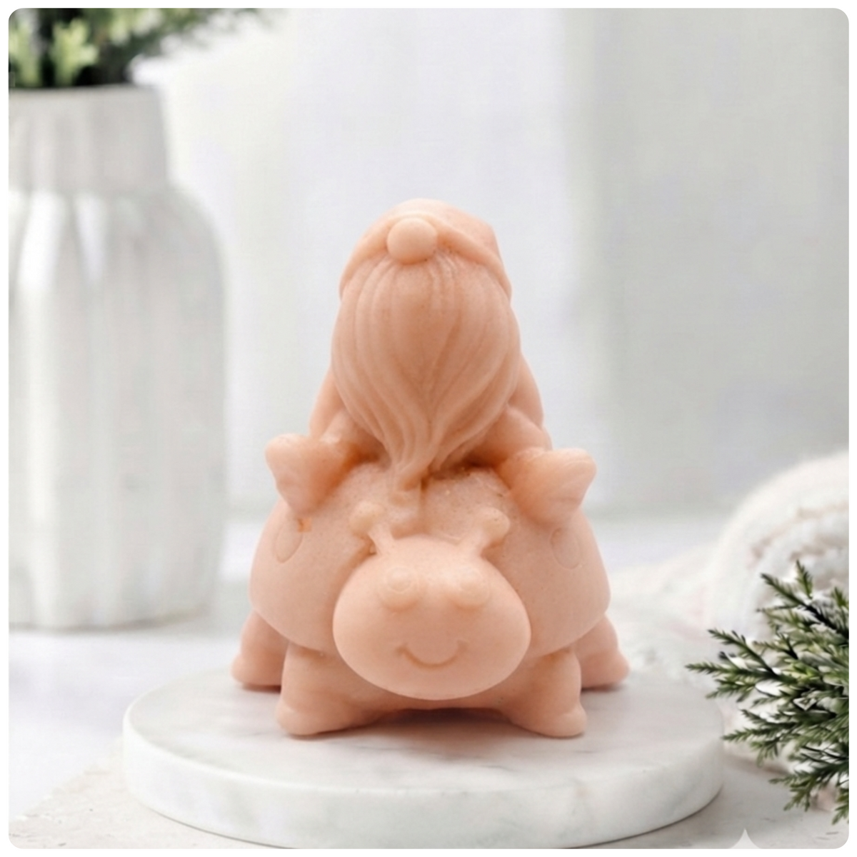 A handmade vegan soap in a warm terracotta-peach tone, sculpted as a whimsical gnome (gonk) with a long, flowing beard sitting on the back of a large, smiling ladybird with visible spots, displayed on a light wooden surface.