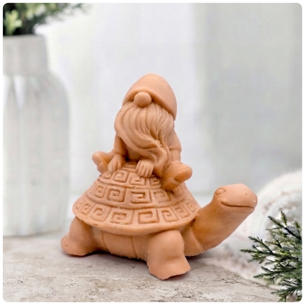 A handmade vegan soap in a natural tone, sculpted as a whimsical gnome (gonk) with a long beard sitting on the back of a large, smiling turtle with a patterned geometric shell.
