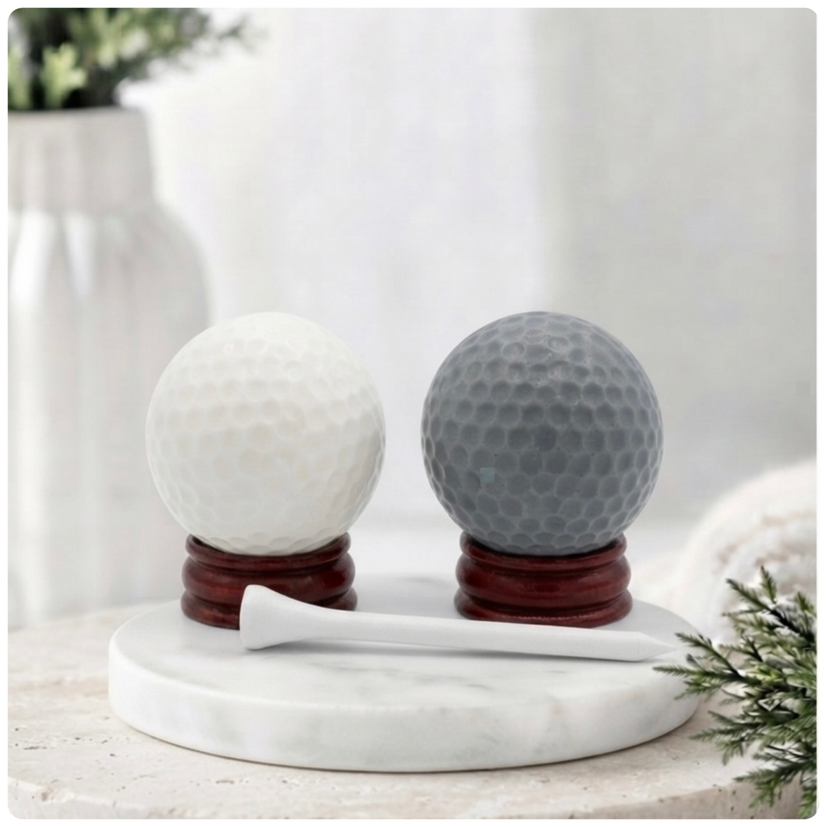 A handmade vegan golf ball soap gift set featuring one white and one grey spherical soap with realistic dimpled textures, displayed on small wooden stands next to a white golf tee and a kraft gift box tied with a red ribbon