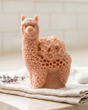 Load image into Gallery viewer, A handmade vegan soap featuring a charming llama or alpaca with a highly textured, fleecy coat and a blanket of intricate flowers across its back, displayed on a light wooden surface in a bright room.
