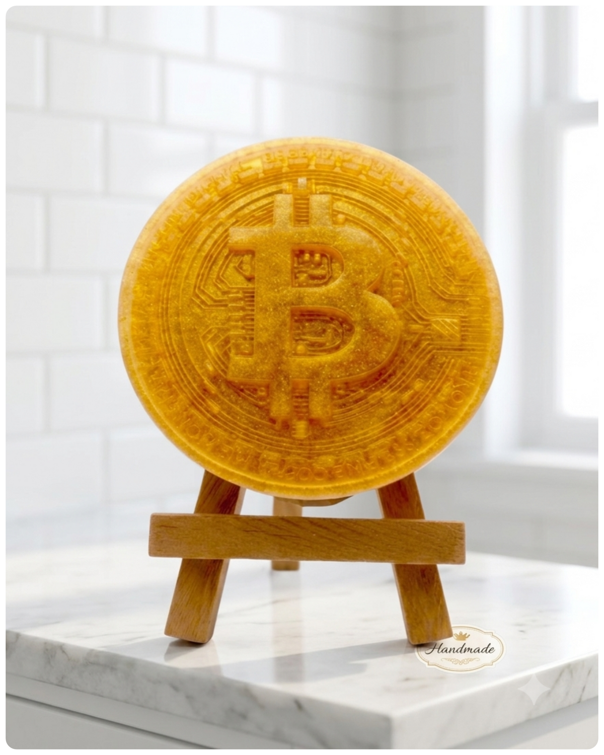 handmade vegan soap in the shape of a Bitcoin coin with a shimmering glitter finish, featuring a detailed relief of the "B" symbol and circuit board patterns, displayed on a small wooden easel in a bright farmhouse decor setting.