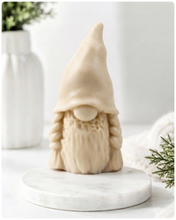 Load image into Gallery viewer, A handmade vegan soap sculpted in the shape of a female gnome (or gonk), featuring a tall, slightly curved hat pulled over the eyes and two thick, textured plaits framing a textured dress, in a natural cream colour.
