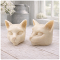 two handmade vegan soaps in the shape of Siamese cat heads, featuring elegant pointed ears and sleek facial features, displayed on a neutral cloth in a bright farmhouse decor setting.