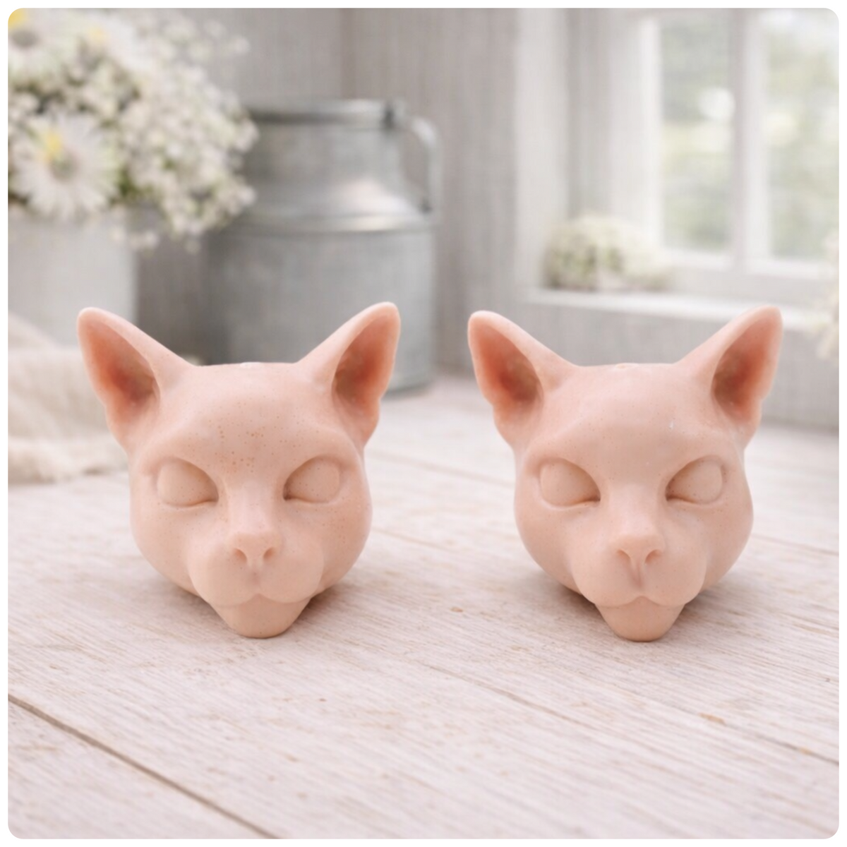 two handmade vegan soaps in the shape of Siamese cat heads, featuring elegant pointed ears and sleek facial features, displayed on a neutral cloth in a bright farmhouse decor setting.