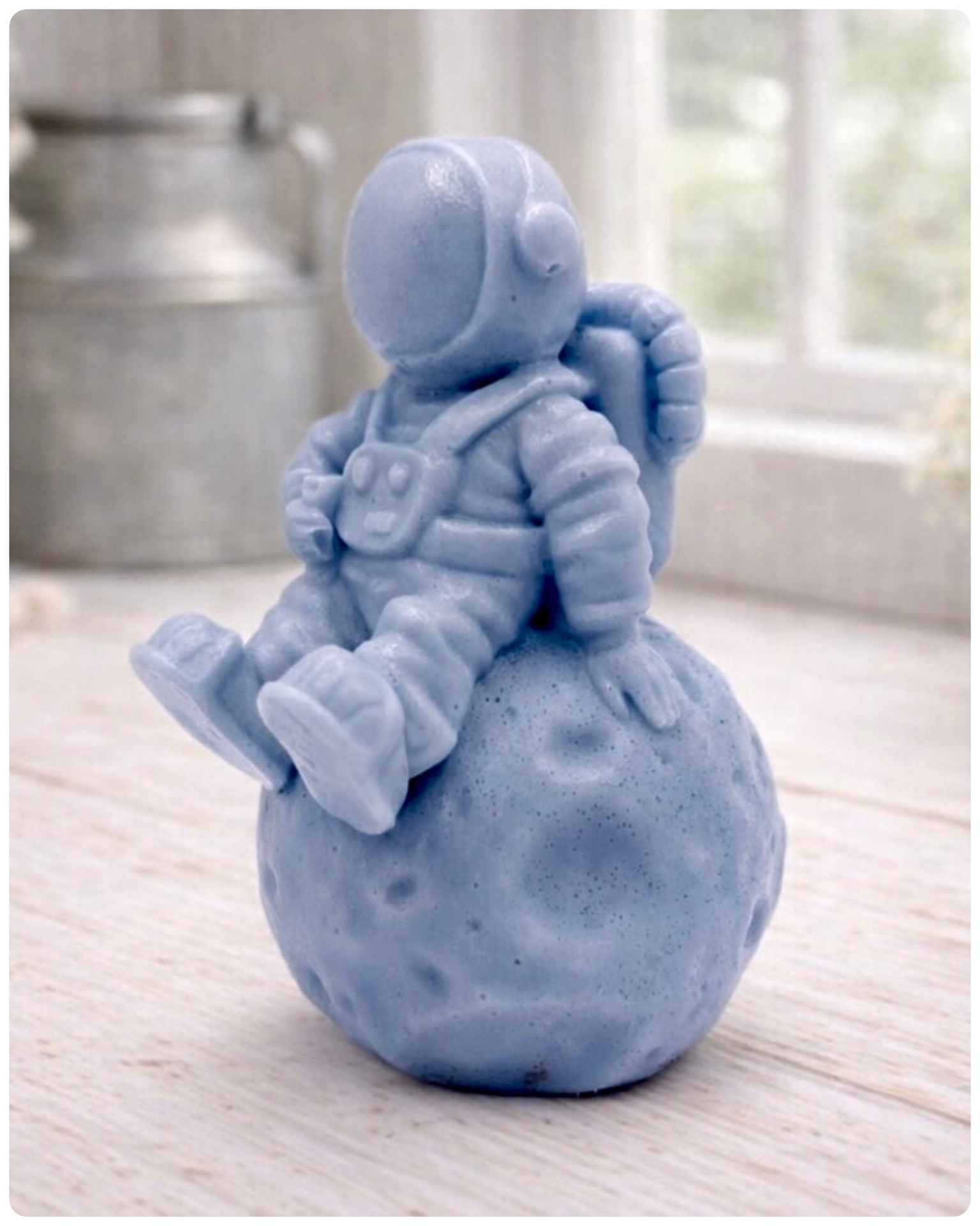 handmade vegan soap in the shape of a realistic astronaut sculpture sitting on the moon, featuring detailed spacesuit textures and craters on the lunar surface, displayed in a bright farmhouse decor setting.