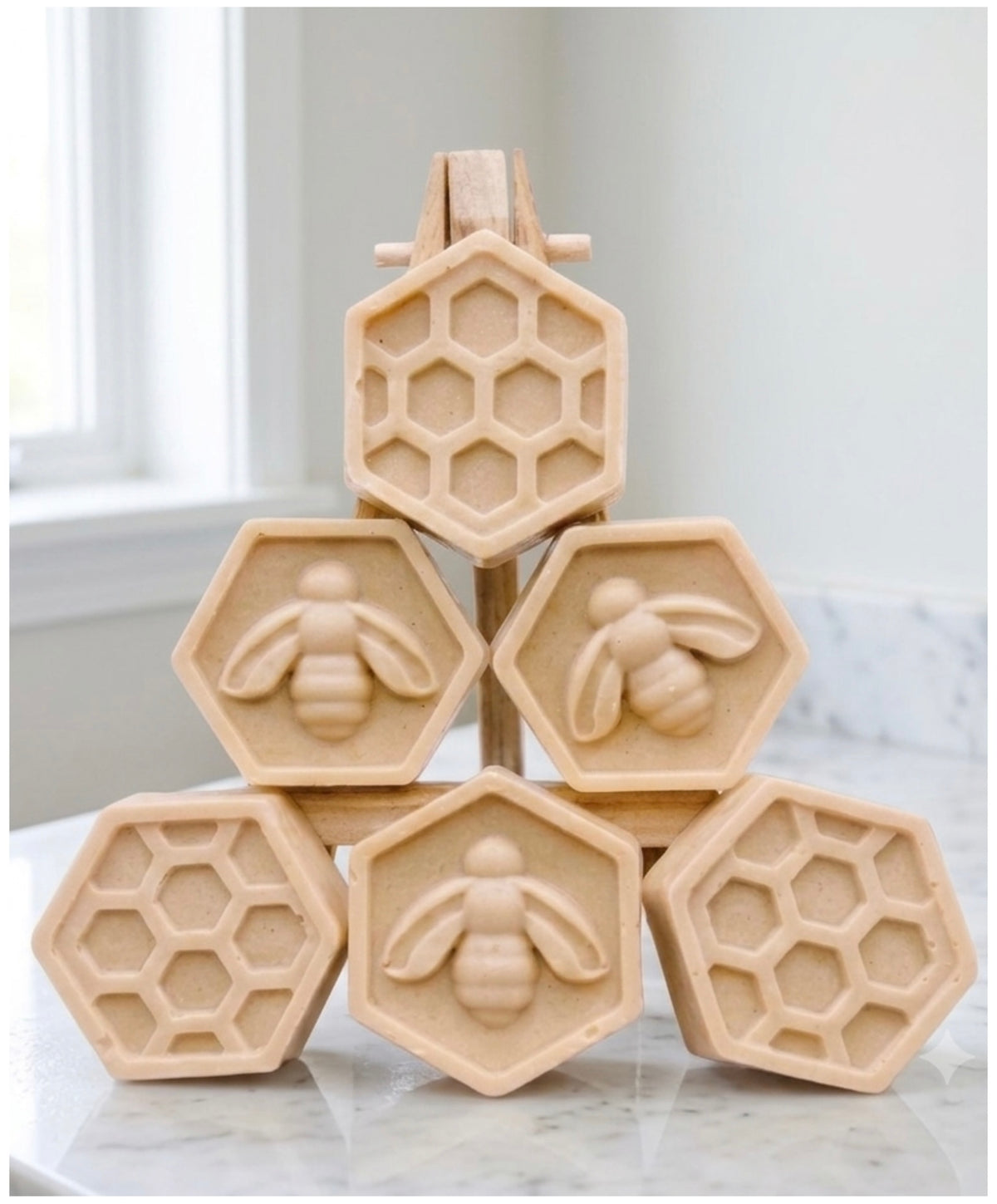 A handmade vegan soap gift set featuring six hexagonal bars stacked in a pyramid on a small wooden easel; some bars show a honeybee relief and others a honeycomb pattern