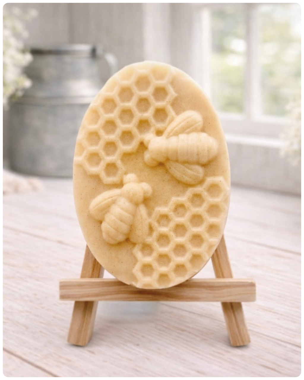 handmade vegan soap featuring an oval relief sculpture of two honey bees crawling on a honeycomb pattern, displayed on a small wooden easel in a bright farmhouse decor setting.