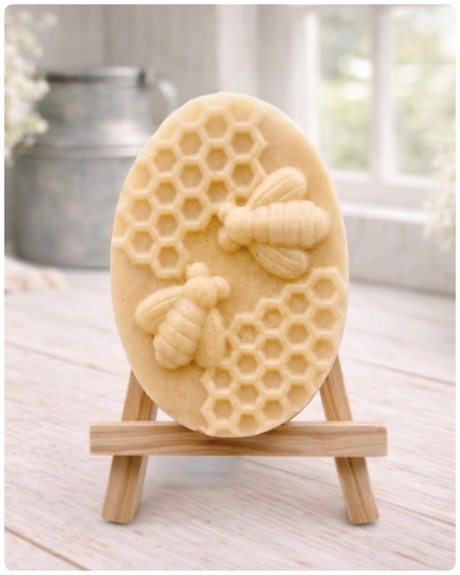 handmade vegan soap featuring an oval relief sculpture of two honey bees crawling on a honeycomb pattern, displayed on a small wooden easel in a bright farmhouse decor setting.