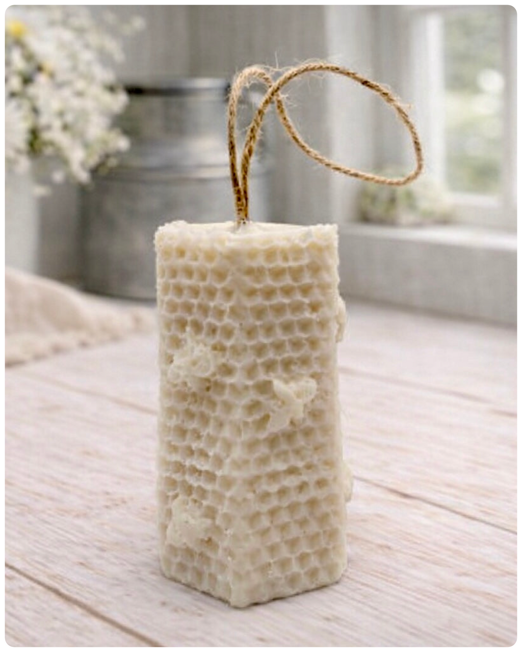 A tall, rectangular handmade vegan soap with a detailed honeycomb texture on all sides and small embossed bees, featuring a natural twine hanging rope, displayed upright on a light wooden surface.