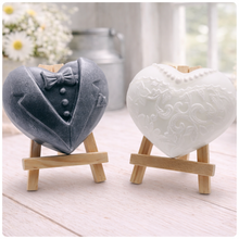 Load image into Gallery viewer, A pair of heart-shaped wedding soaps shaped like a bride's white lace dress and a groom's grey tuxedo, displayed on small wooden easels. Gift boxed ready to give. 
