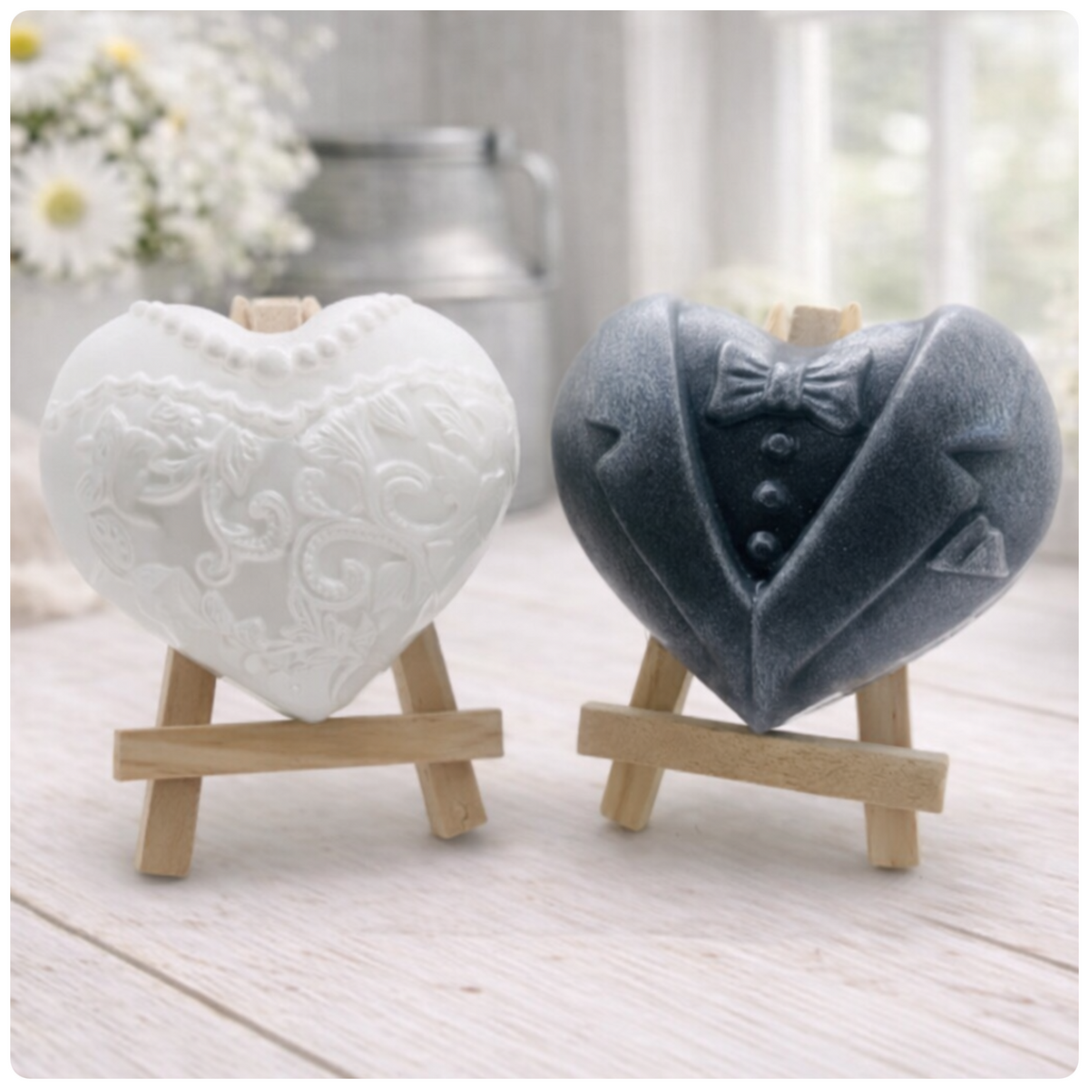 A pair of heart-shaped wedding soaps shaped like a bride's white lace dress and a groom's grey tuxedo, displayed on small wooden easels. Gift boxed ready to give. 