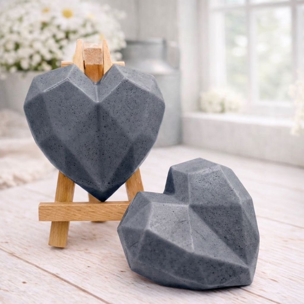 Two handmade vegan soaps in a contemporary geometric heart shape, with one displayed on a small wooden easel, set against a bright farmhouse decor background with white flowers.