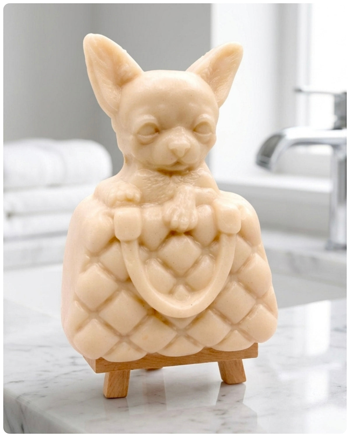 A highly detailed handmade vegan soap in a speckled grey marble finish, sculpted as a small chihuahua puppy with large ears peeking out from inside a quilted designer-style handbag, displayed on a miniature wooden easel.