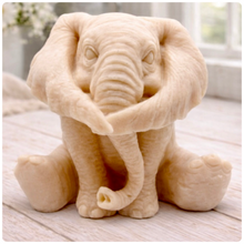 Load image into Gallery viewer, A crisp product photograph of a detailed, grey artisan bar of soap intricately moulded into the shape of a sitting baby elephant. The elephant is depicted holding its trunk with its front legs crossed in a "hear no evil" or hugging pose, showcasing realistic skin textures, expressive eyes, and large ears.
