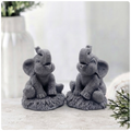 A charming gift set of two handmade vegan soaps, one sculpted as a sitting baby elephant with a trunk raised in a greeting and the other as a smaller standing calf, displayed on a light wooden surface in a bright farmhouse setting.