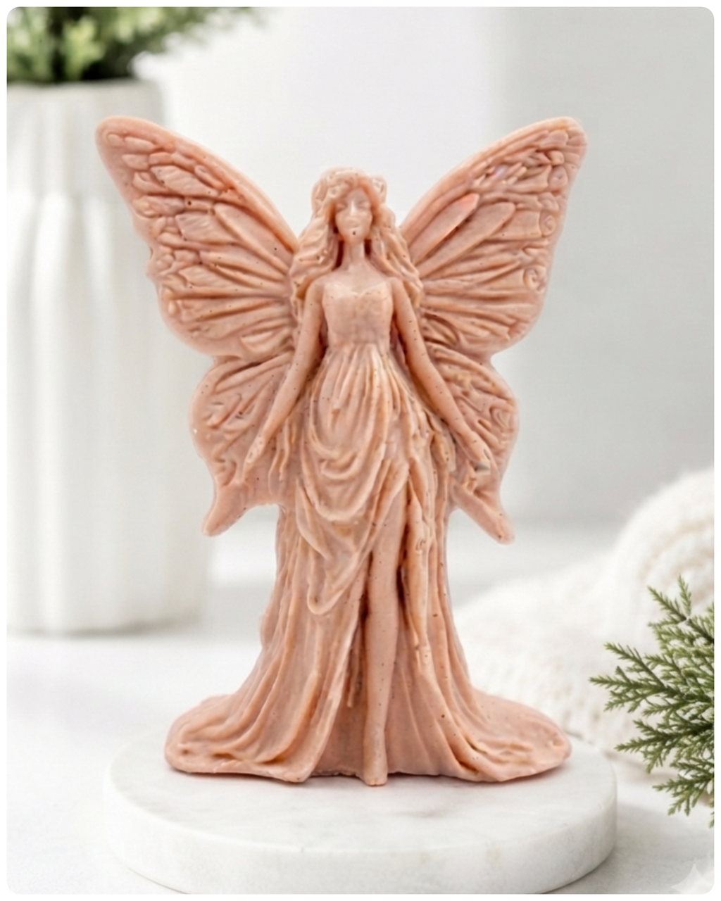A detailed handmade vegan soap featuring an elegant fairy with large, intricate butterfly-style wings, a flowing gown, and long hair, standing against a bright farmhouse window background.