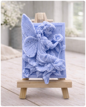Load image into Gallery viewer, A rectangular handmade vegan soap, featuring a high-relief carving of a seated fairy with large, detailed wings holding a single blossom, displayed on a miniature wooden easel.
