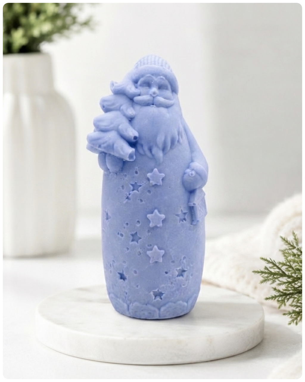 handmade vegan soap sculpted into a tall figure of Father Christmas wearing star-patterned robes, holding a small Christmas tree in one arm and a lantern in the other, set in a bright farmhouse window.