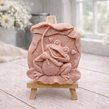 Load image into Gallery viewer, A rectangular handmade vegan soap featuring a high-relief carving of a cheerful, smiling frog sitting on a large lilypad and holding the stem of a leaf over its head like an umbrella.
