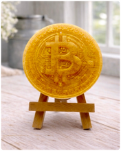 Load image into Gallery viewer, handmade vegan soap in the shape of a Bitcoin coin with a shimmering glitter finish, featuring a detailed relief of the "B" symbol and circuit board patterns, displayed on a small wooden easel in a bright farmhouse decor setting.
