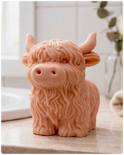 Load image into Gallery viewer, A detailed handmade vegan soap in a sculpted in the shape of a highland cow with characteristic long, wavy fur, horns, and a friendly face, displayed on a light wooden surface
