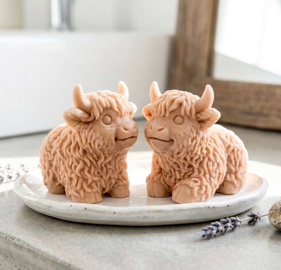 A highly detailed handmade vegan soap sculpted in the shape of a highland cow with long, flowing fur texture, a sweet face with a large snout, and prominent horns, displayed on a light wooden surface in a bright farmhouse setting.