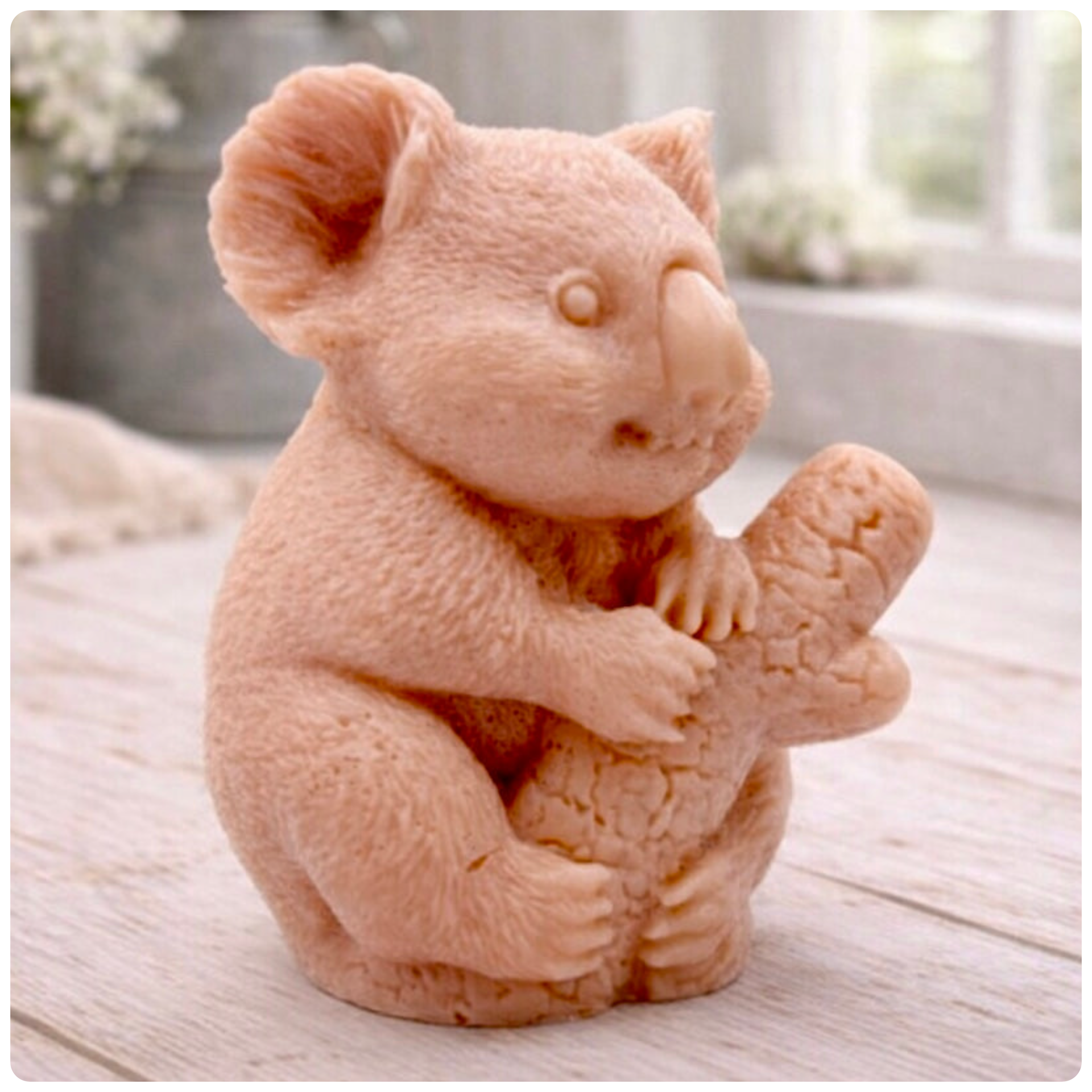 A highly detailed handmade vegan soap in a sculpted in the shape of a realistic koala bear sitting upright and clutching a textured eucalyptus branch, displayed on a light wooden surface in a bright farmhouse background 