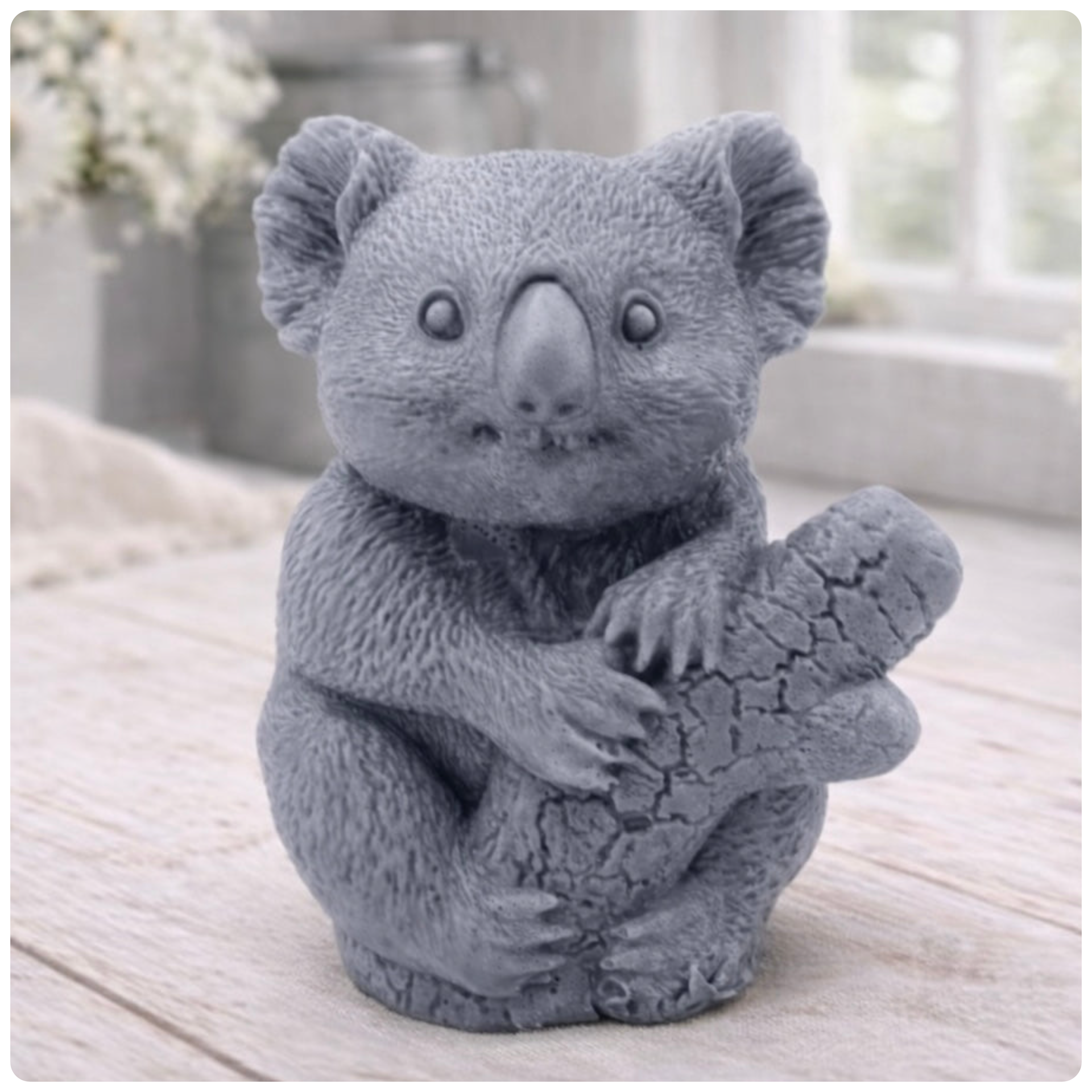 A highly detailed handmade vegan soap in a sculpted in the shape of a realistic koala bear sitting upright and clutching a textured eucalyptus branch, displayed on a light wooden surface in a bright farmhouse background 