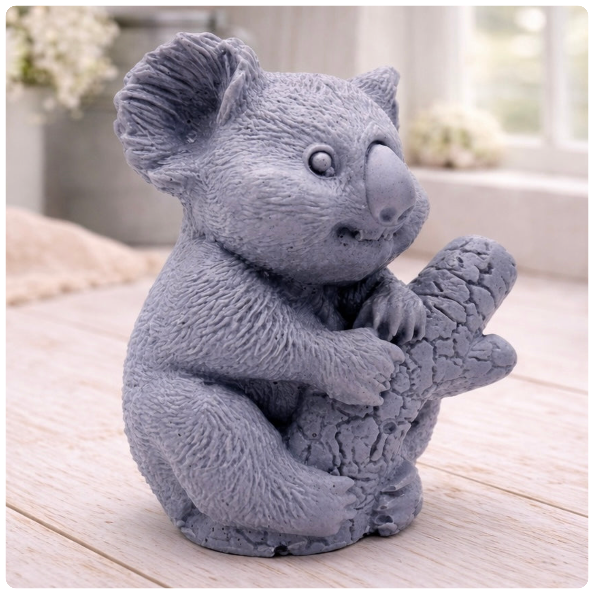 A highly detailed handmade vegan soap in a sculpted in the shape of a realistic koala bear sitting upright and clutching a textured eucalyptus branch, displayed on a light wooden surface in a bright farmhouse background 