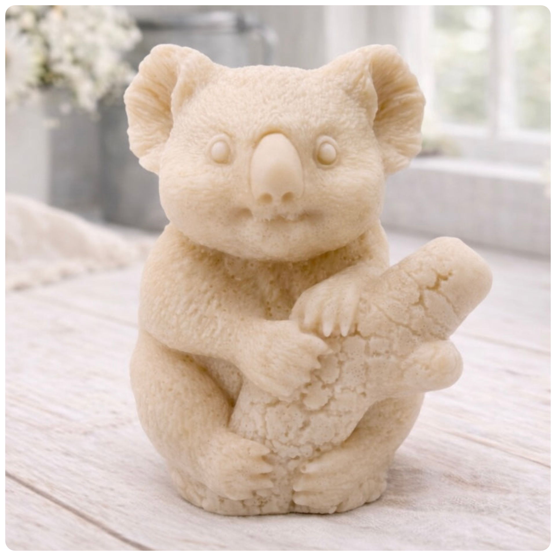 A highly detailed handmade vegan soap in a sculpted in the shape of a realistic koala bear sitting upright and clutching a textured eucalyptus branch, displayed on a light wooden surface in a bright farmhouse background 