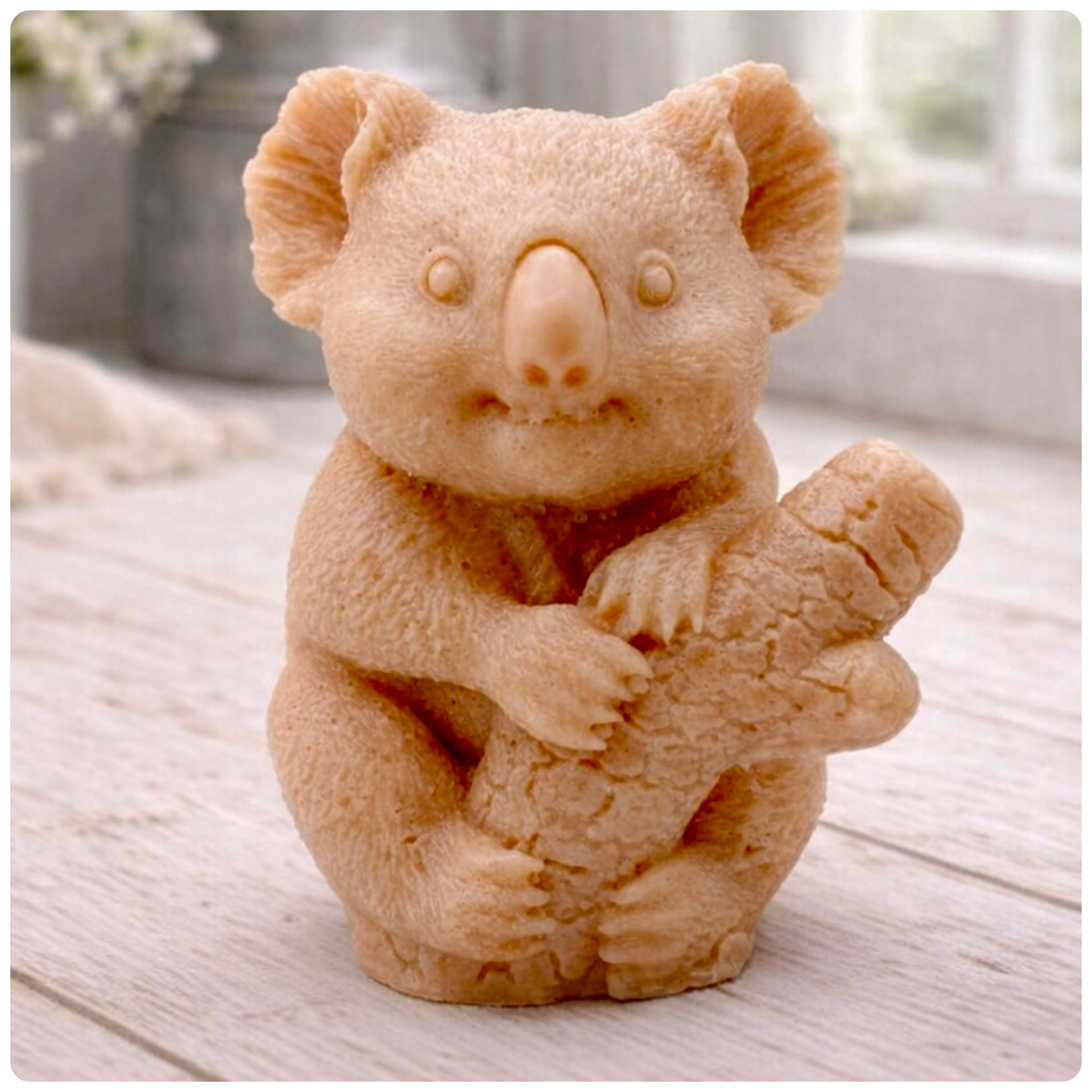 A highly detailed handmade vegan soap in a sculpted in the shape of a realistic koala bear sitting upright and clutching a textured eucalyptus branch, displayed on a light wooden surface in a bright farmhouse background 