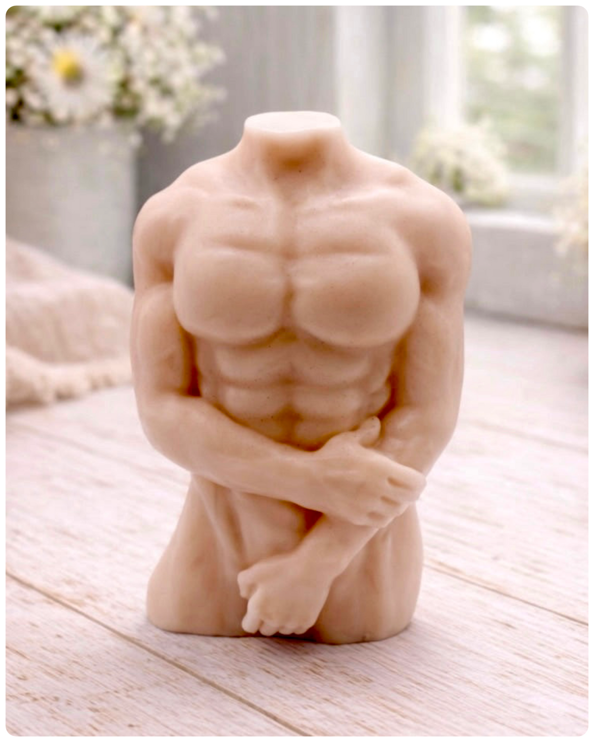 A handmade vegan soap sculpted into a detailed male torso with defined chest and abdominal muscles, finished in a soft tone and displayed in a bright farmhouse setting.