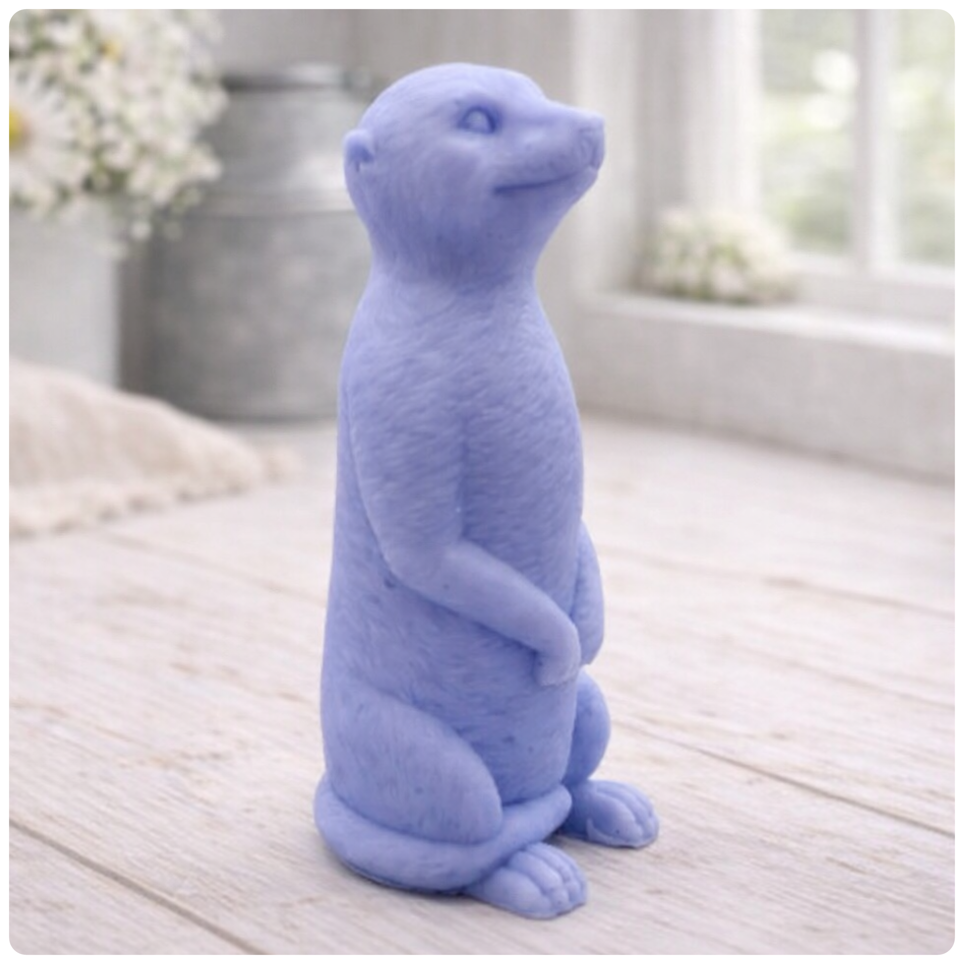 A highly detailed handmade vegan soap, sculpted in the shape of a realistic meerkat standing upright in its iconic sentinel pose, featuring textured fur and a curious facial expression, displayed on a light wooden surface.