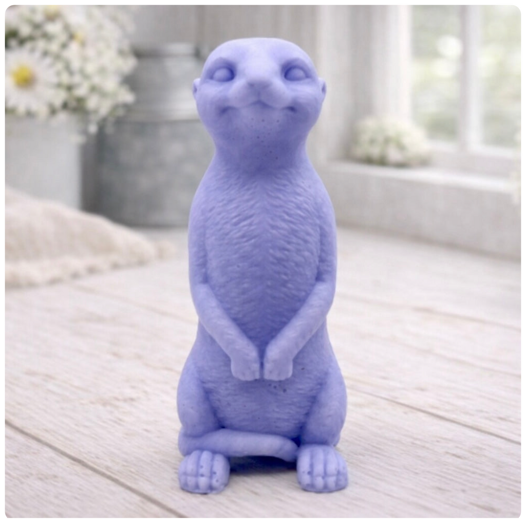 A highly detailed handmade vegan soap, sculpted in the shape of a realistic meerkat standing upright in its iconic sentinel pose, featuring textured fur and a curious facial expression, displayed on a light wooden surface.
