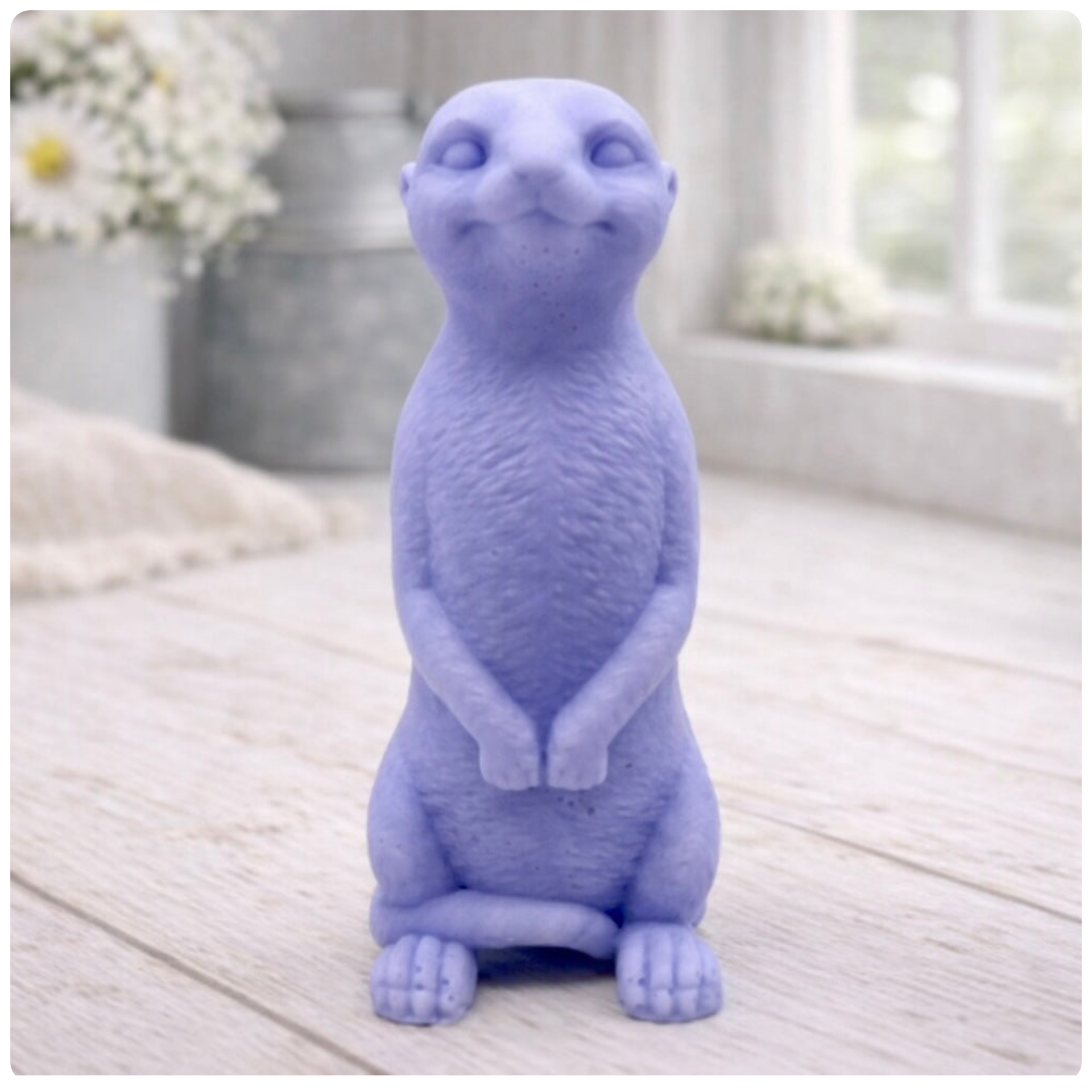 A highly detailed handmade vegan soap, sculpted in the shape of a realistic meerkat standing upright in its iconic sentinel pose, featuring textured fur and a curious facial expression, displayed on a light wooden surface.