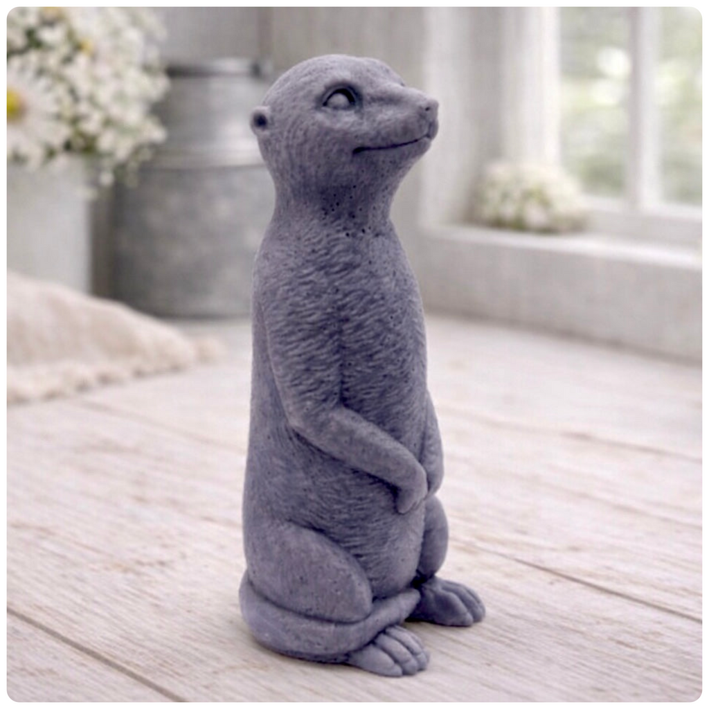 A highly detailed handmade vegan soap, sculpted in the shape of a realistic meerkat standing upright in its iconic sentinel pose, featuring textured fur and a curious facial expression, displayed on a light wooden surface.