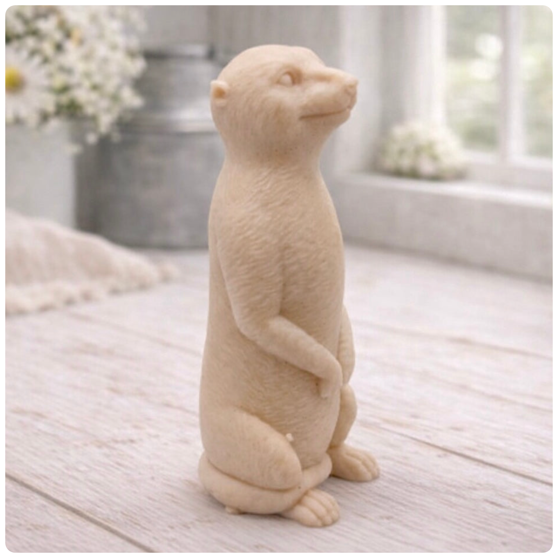 A highly detailed handmade vegan soap, sculpted in the shape of a realistic meerkat standing upright in its iconic sentinel pose, featuring textured fur and a curious facial expression, displayed on a light wooden surface.