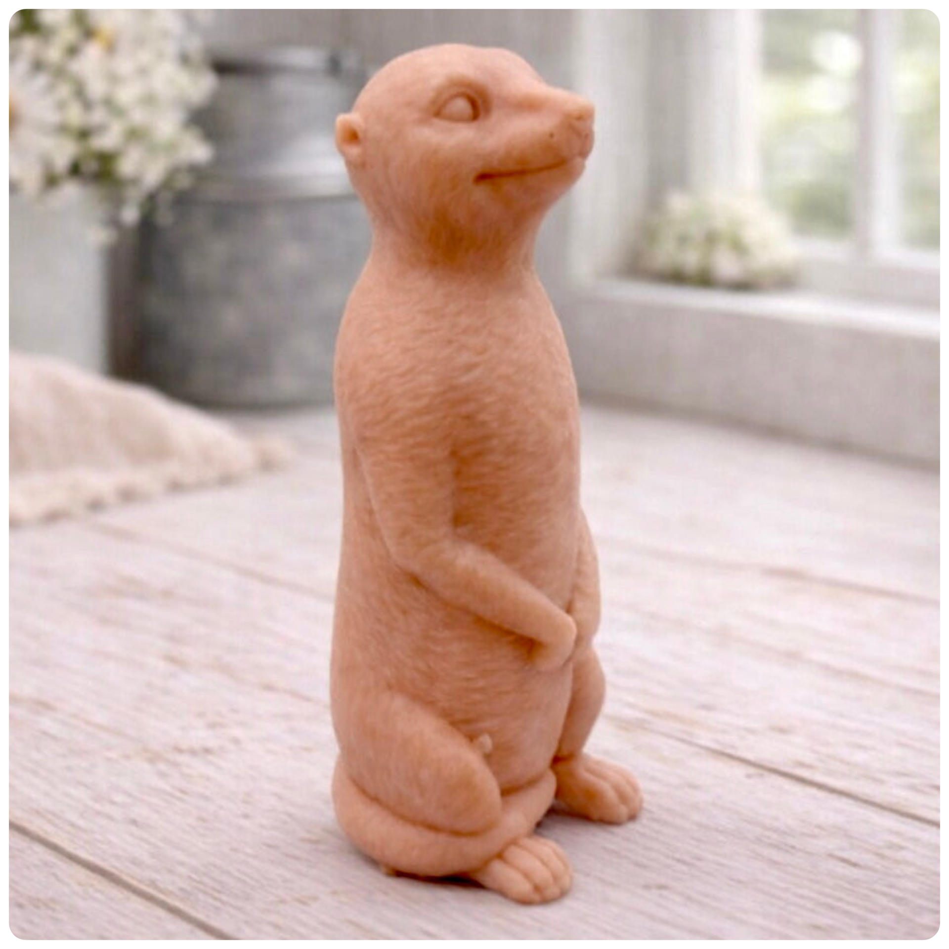 A highly detailed handmade vegan soap, sculpted in the shape of a realistic meerkat standing upright in its iconic sentinel pose, featuring textured fur and a curious facial expression, displayed on a light wooden surface.