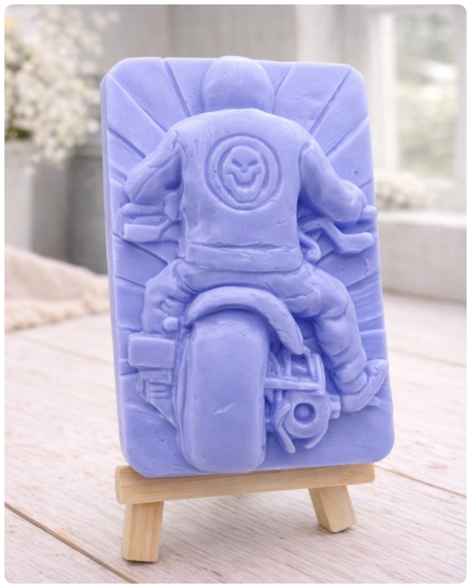 detailed handmade vegan soap gift featuring a motorcycle rider with a skull emblem on their jacket, displayed on a wooden easel against a whimsical farmhouse decor background
