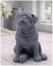 Load image into Gallery viewer, A detailed handmade vegan soap sculpted in the shape of a sitting pug dog with characteristic facial wrinkles and a tilted head, in a natural tone, displayed on a light wooden surface.
