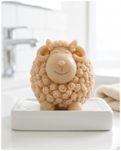 Load image into Gallery viewer, A highly detailed handmade vegan soap sculpted in the shape of a sturdy ram with a thick coat of tight, curly wool and large, elegant curved horns, displayed on a light wooden surface in a bright farmhouse setting.
