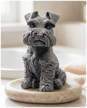 Load image into Gallery viewer, A detailed handmade vegan soap sculpted in the shape of a sitting Schnauzer dog with characteristic fluffy eyebrows and beard, in a natural colour, set against a bright window and white flowers. By soap Simple creations 
