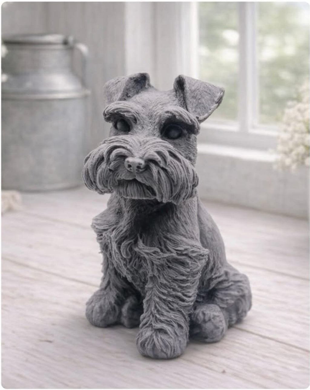 A detailed handmade vegan soap sculpted in the shape of a sitting Schnauzer dog with characteristic fluffy eyebrows and beard, in a natural colour, set against a bright window and white flowers. By soap Simple creations 