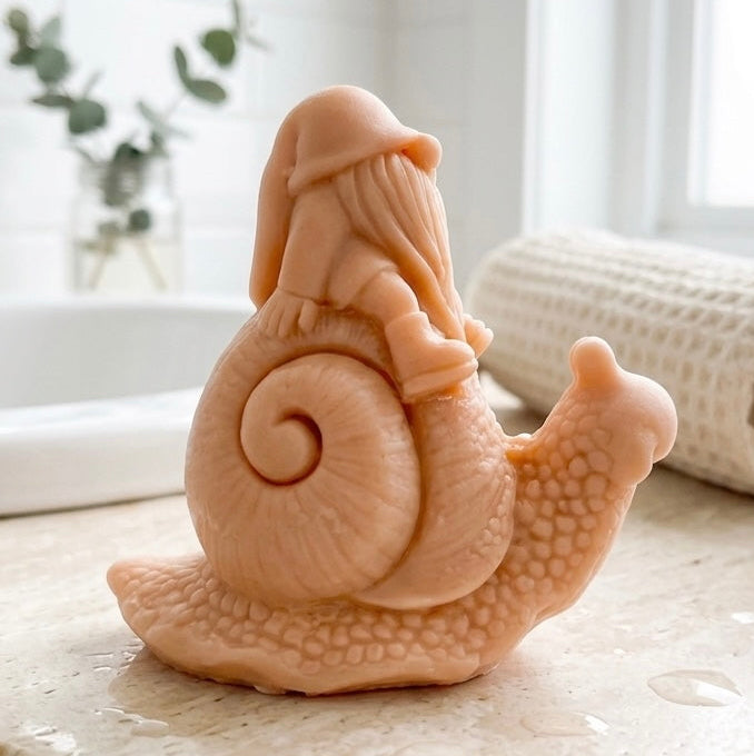 A handmade vegan soap gift, sculpted as a whimsical gnome (gonk) with a tall, slouchy hat and a long beard, sitting on the shell of a large snail with a textured, bumpy body.