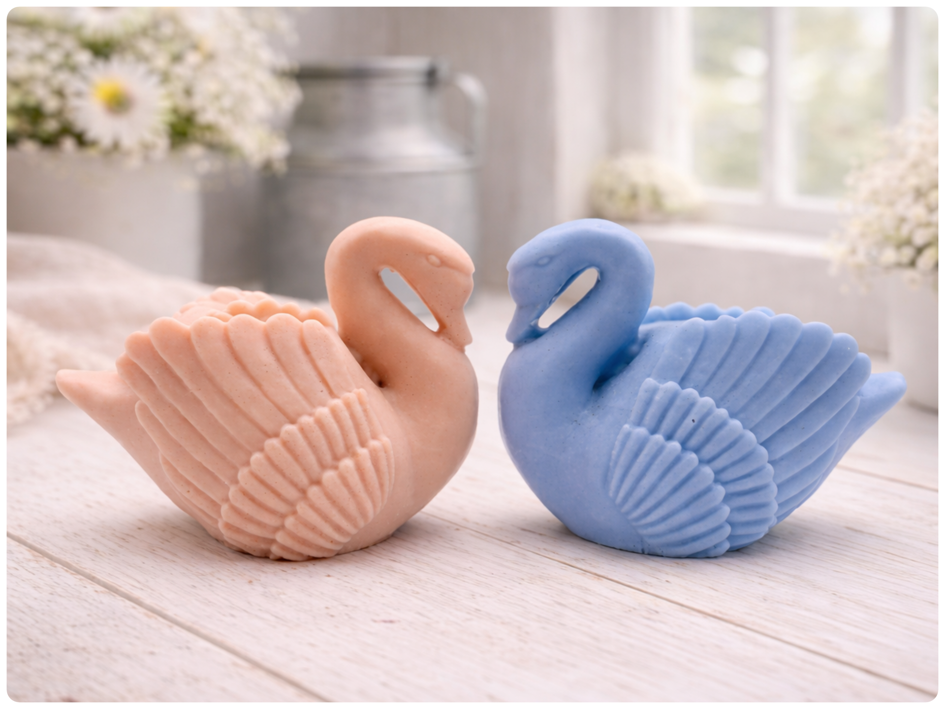 Two swan-shaped soaps, one pink and one blue, on a wooden surface with a blurred floral background.
